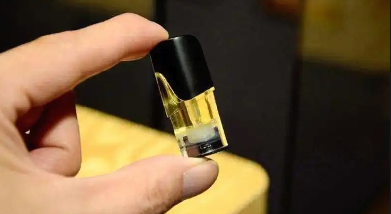 手指拿著裝有黃色煙油的透明電子煙煙彈，可見黑色吸嘴與內部結構